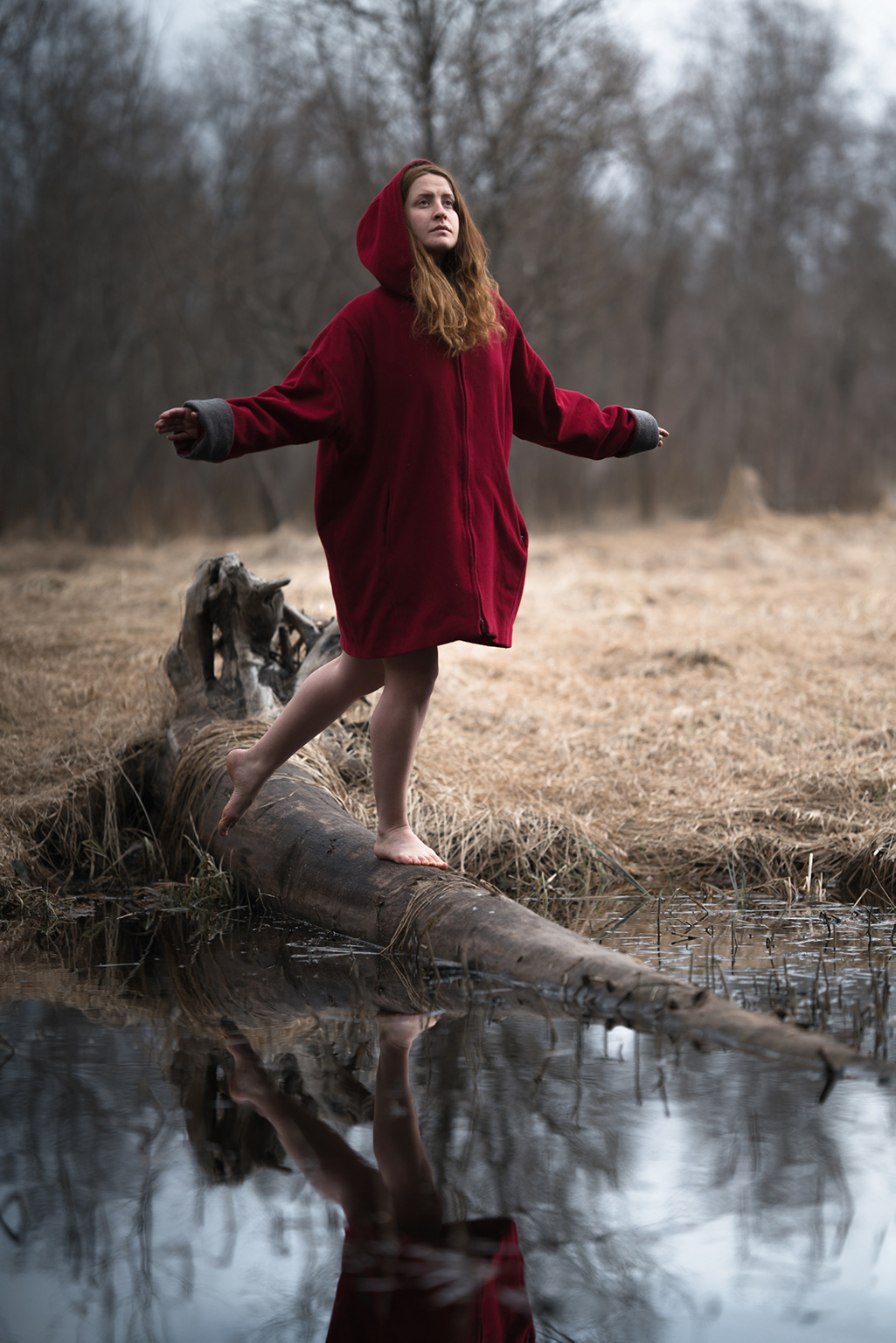 Jessie Lewis Skoglund i röd luva, balanserandes på en trädstam i en bäck